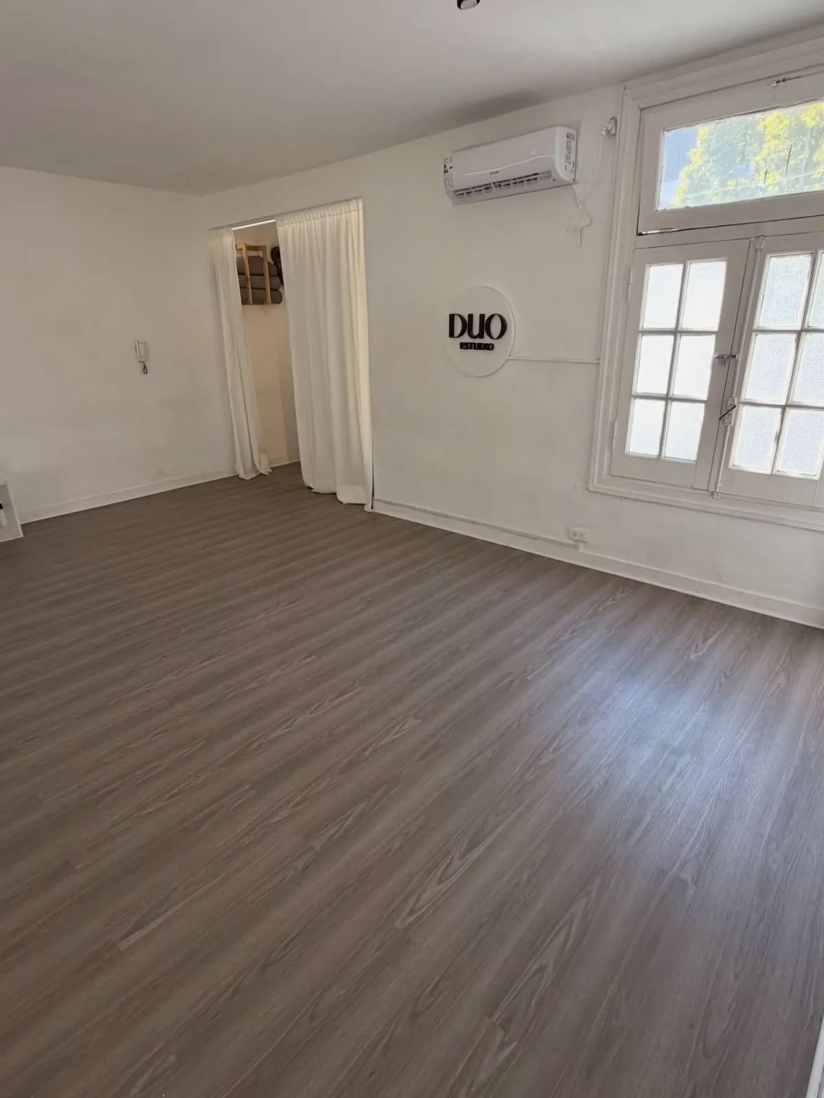 Sala de Duo Estudio con piso de madera, ventanas con luz natural y el logo en la pared